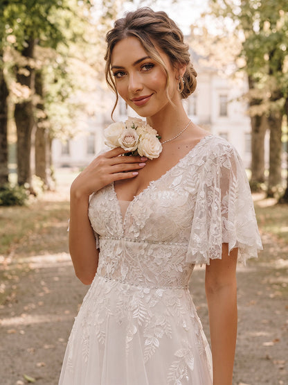 Robe de mariée en tulle, coupe trapèze/princesse, col en V, manches courtes, longueur au sol, avec applications et volants.